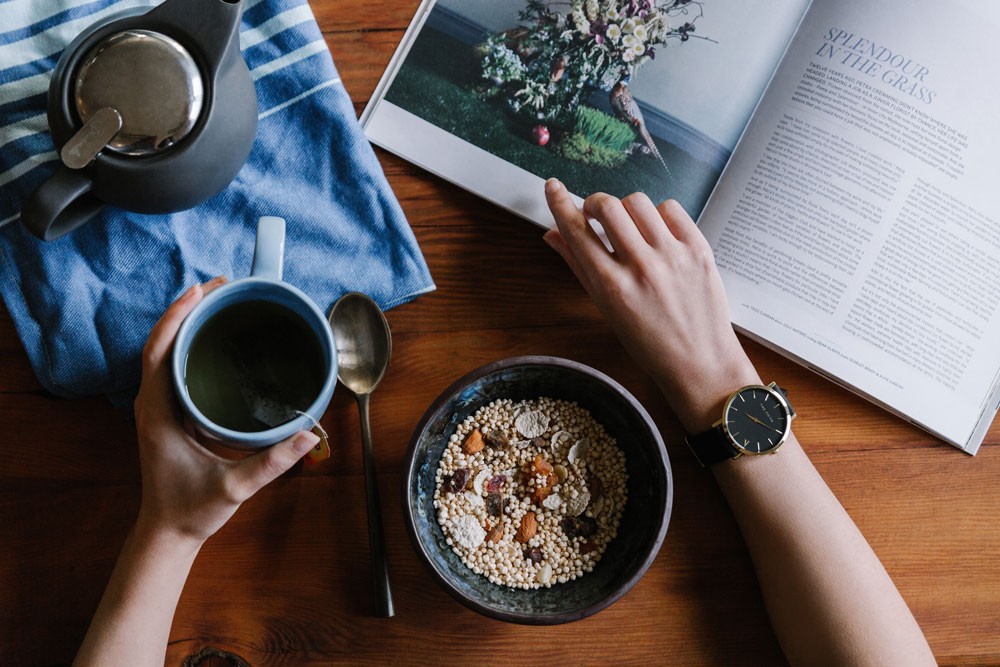 chica sentada en una mesa con un bowl, un café y un libro